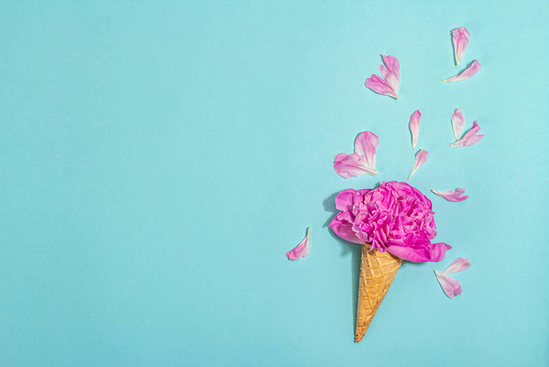 青い背景に牡丹のアイスクリームワッフルコーン。花の花びら、夏のコンセプト。ロマンチックなスタイル、お祝いのカード、ハードライト、暗い影、トップビュー - 写真・画像