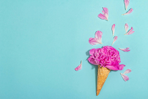 Conos de gofre de helado con peonía sobre fondo azul. Pétalos de flores, concepto de verano. Estilo romántico, tarjeta festiva, luz dura, sombra oscura, vista superior - Foto, imagen