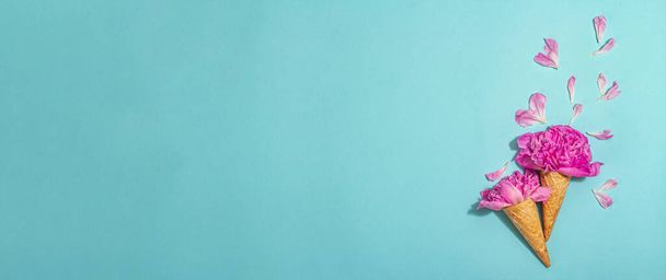 Cones de waffle de sorvete com peônia em fundo azul. Pétalas de flores, conceito de verão. Estilo romântico, cartão festivo, luz dura, sombra escura, formato de banner - Foto, Imagem