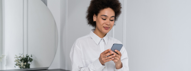 smiling african american woman messaging on smartphone at home, banner - Foto, imagen