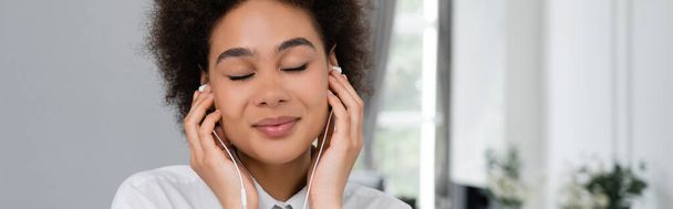onnellinen afrikkalainen amerikkalainen nainen, jolla on suljetut silmät kuuntelemassa musiikkia langallisissa kuulokkeissa, banneri  - Valokuva, kuva