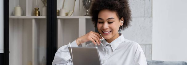 happy african american woman in wired earphones holding digital tablet while watching movie, banner - Foto, Imagen