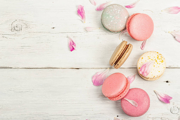 Macarons with peony flower petals on a white wooden background. Sweet dessert, colorful and pastel colors. Romantic style, festive card, flat lay, top view - Photo, image