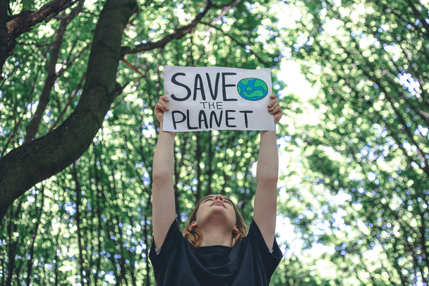 Плакат в призыве спасти планету в женских руках в лесу, концепция ухода за природой, уборки, переработки и экологии. - Фото, изображение