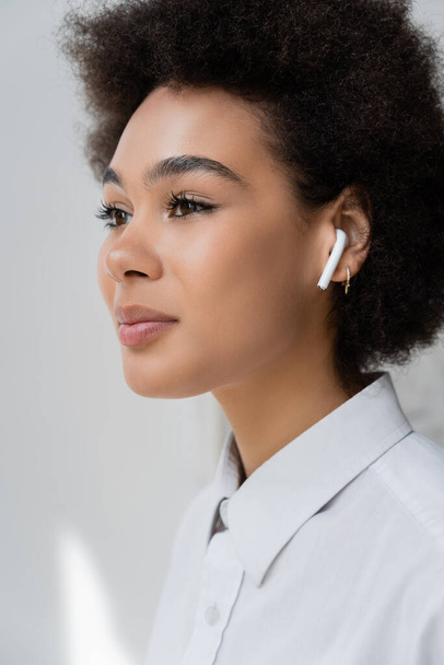 portrait of curly african american woman listening music in wireless earphone - Photo, Image