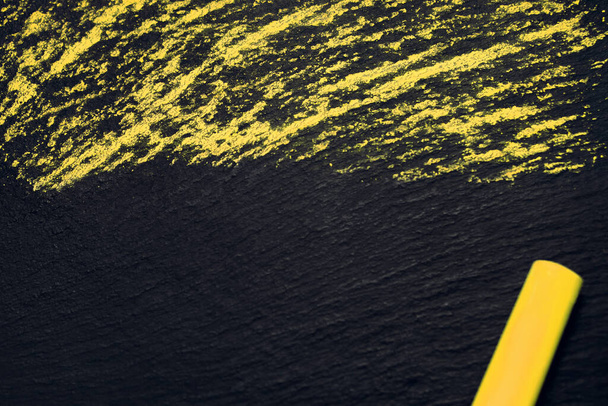 Gelbe Kreide auf schwarzem Grungy Board mit freier Textfläche. Ein Bild als Hintergrund mit leerem Raum für Text und gelber Kreide in der Ecke. Einfaches horizontales Bild mit Kreide - Foto, Bild