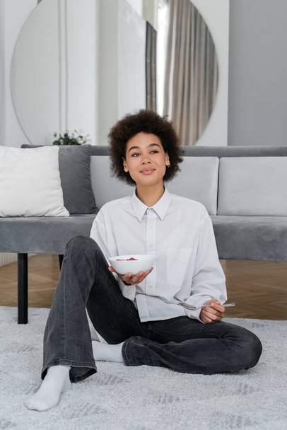happy and young african american woman holding bowl with tasty breakfast  - Foto, imagen