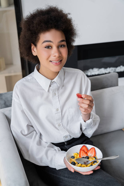 happy african american woman holding bowl with corn flakes and fresh strawberry - Photo, Image