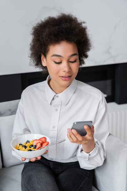 göndör afro-amerikai nő gazdaság tál reggelivel és okostelefon - Fotó, kép