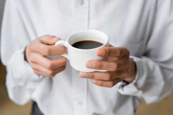 cropped view of woman holding cup of black and hot coffee in hands - Foto, Imagem