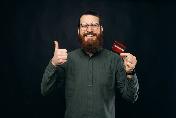 Hey c'est une nouvelle carte de crédit, heureux jeune homme hipster montrant pouce vers le haut geste et carte de débit. - Photo, image