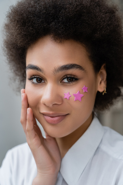 portrait of smiling african american woman with decorative purple stars on cheek  - Photo, Image
