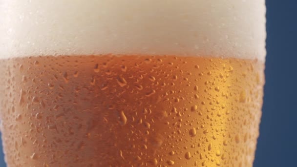 Druppels op een glas bier en schuimig bier. Een glas bier draait langzaam om zijn as. en de druppel stroomt op het glas, Macro schieten. Sluiten.  - Video