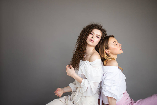 Two fashion female models on a grey background studio portrait of of two young stylish girls posing - Фото, изображение