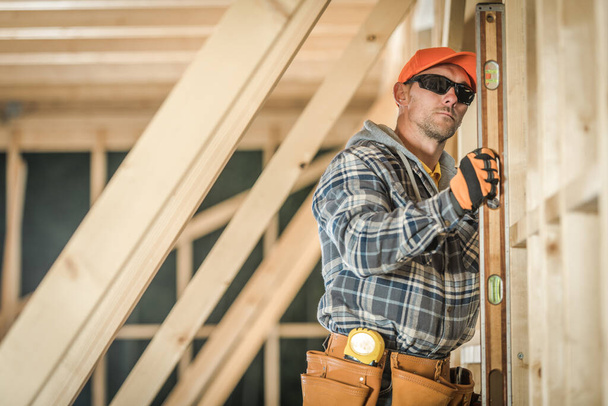Caucasian Construction Worker Verifying the Straightness of Freshly Built Wooden House Roof Skeleton Using His Building Spirit Level Tool. Construction Site Background. - Foto, Bild
