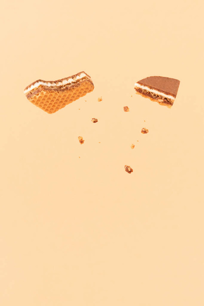 Bitten wafer cookie with crumbs against pastel beige background. Layered wafer with chocolate, milk and hazelnuts. Creative food concept. - Fotó, kép