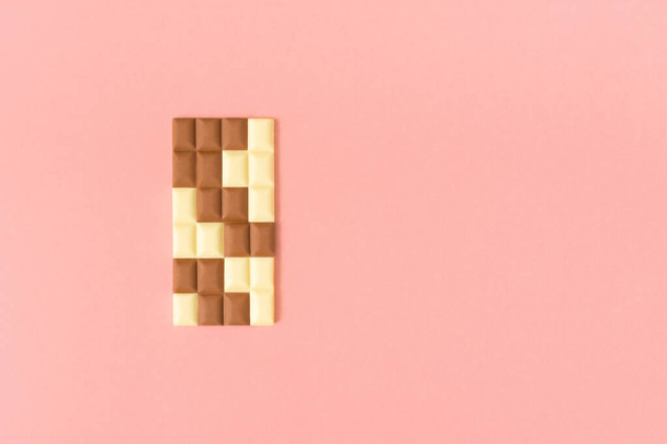 Black and white pieces of chocolate bar on a pastel pink background. Minimal food aesthetic. Creative puzzle concept. - Foto, imagen