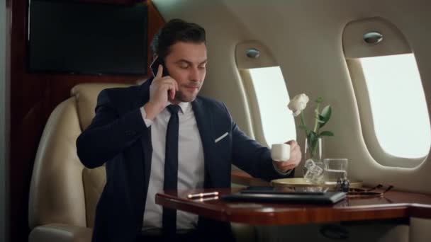 Занятой человек заканчивает телефонный разговор на роскошном самолете. Сосредоточенный менеджер, пьющий кофе в самолете бизнес-класса. Красивый бизнесмен заканчивает мобильный разговор. Успешный финансовый аналитик - Кадры, видео