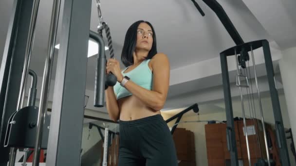 Tríceps de cuerda tirada hacia abajo. Una mujer deportiva está haciendo ejercicios de entrenamiento diario en el gimnasio. - Imágenes, Vídeo