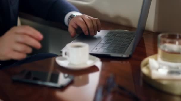 Close-up Hand-Tippen Laptop beginnt Online-Videokonferenz auf Flugreise. Unbekannter erfolgreicher Mann winkt Gesprächspartner in Business-Klasse zu. Geschäftsmann nimmt Kaffeetasse im Flugzeug mit - Filmmaterial, Video