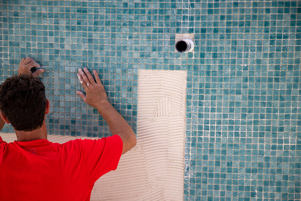 Trabajador reparando la piscina, la colocación de azulejos de color turquesa gresite.   - Foto, imagen