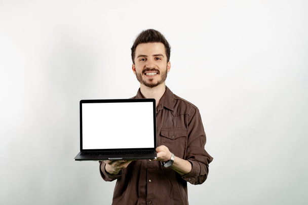 幸せなカジュアル男身に着けているカジュアル服ポージング上の隔離された白い背景保持ラップトップPCコンピュータで空の画面. - 写真・画像