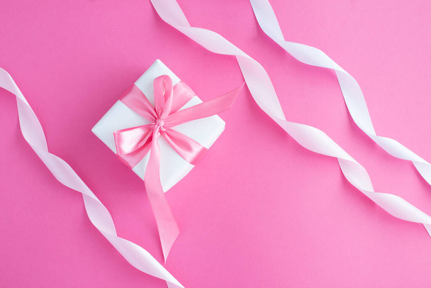 Gift box with tied pink bow and ribbon on the pink background. Closeup. Top view. - Фото, изображение