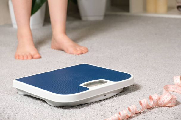 Bare πόδια και μια μπλε κλίμακα δαπέδου με ταινία μέτρησης εκατοστών, η έννοια της απώλειας βάρους - Φωτογραφία, εικόνα