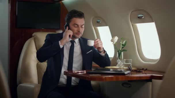 Europese zakenman die mobiele telefoon spreekt. Succesvolle ceo zakenreis bespreken partner deal. Zelfverzekerde stijlvolle man die praat over cel kijkend vliegtuigraam. Drukke passagier drinkt koffie. - Video