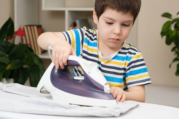 Um menino de 4 anos aprende a segurar um ferro, roupas de ferro em uma tábua de engomar. Ajudante, ajude as crianças a cuidar da casa - Foto, Imagem