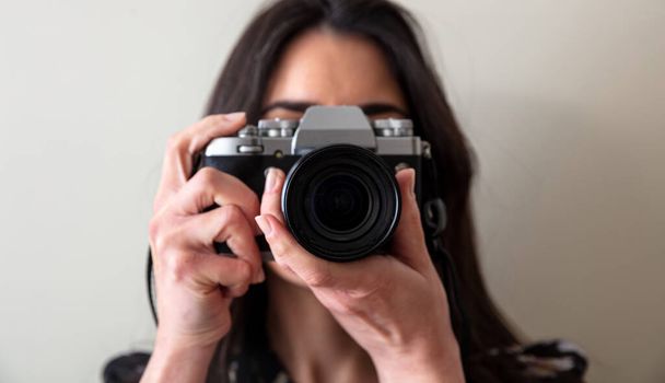 Young woman holding photo camera is shooting your picture. Girl photographer focus at you, close up view - Foto, Imagen