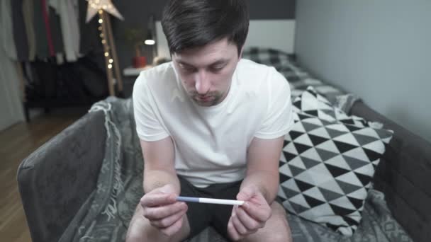 An unhappy young man looks at a pregnancy test. Upset guy with problems from his girlfriends pregnancy. The male is depressed about the result of the pregnancy test. I didnt become father again.  - Footage, Video