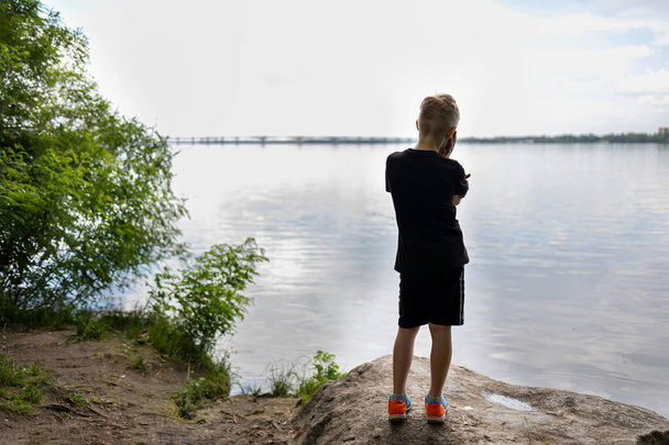 boy traveler stands with his back on a stone and looks pensively at the river - 写真・画像