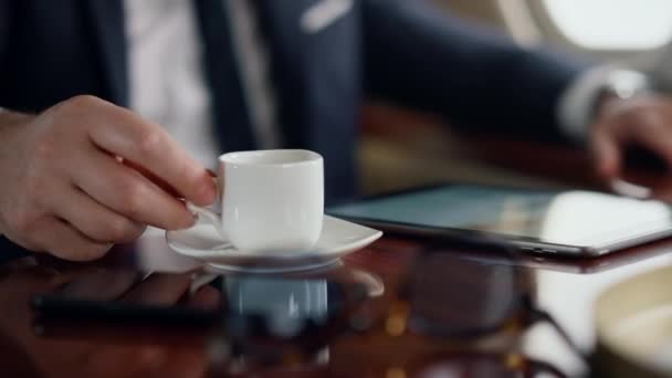 Mann genießt Kaffeetrinken auf Geschäftsreise. Nahaufnahme Hand nimmt Teetasse im Flugzeug. Unbekannte Geschäftsmann trinken Schluck Schluck legte Tasse zurück in Luxuskabine. Entspannte Erholung nach der Arbeit mit dem Tablet - Filmmaterial, Video