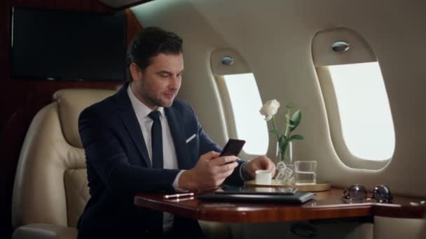 Europese zakenman typt telefoon op vliegtuigreis. Zelfverzekerde manager die koffie drinkt in een luxe jet. Succesvolle man die surf internet sms 't in pak. Happy gentleman check e-mail gebruik smartphone - Video