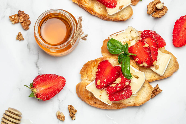 Bruschetta mit Erdbeeren, Käse-Camembert-Nüssen und Honig auf hellem Hintergrund. Essen Rezept Hintergrund. Nahaufnahme. - Foto, Bild