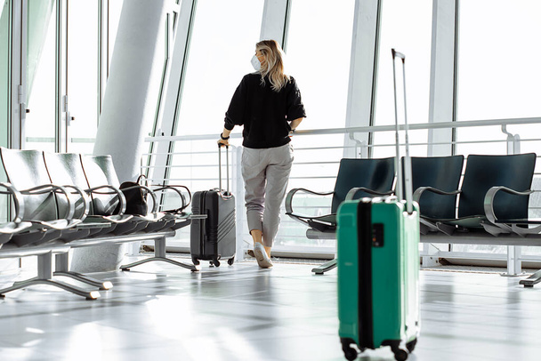 Travel tourist woman standing with luggage watching at airport window. Unrecognizable woman. Travel, lifestyle. Passenger waiting for boarding gate before departure. Travel lifestyle.  - Zdjęcie, obraz