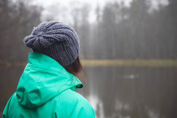 Brunette in winter jacket looking at a small pond near Opava, Czech Republic. Green and blue winter jacket. Lifestyle. - Fotografie, Obrázek