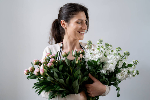 WOMAN florist EMBRACING a bunch of white and pink flowers on white background indoors - Foto, Bild