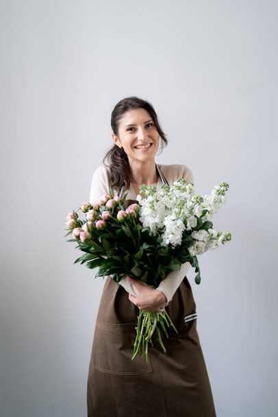 WOMAN florist EMBRACING a bunch of white and pink flowers on white background indoors - Zdjęcie, obraz