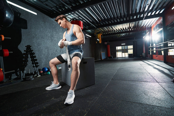 Серьезный сосредоточенный мускулистый молодой спортсмен, обмотавший правую руку эластичной повязкой - Фото, изображение