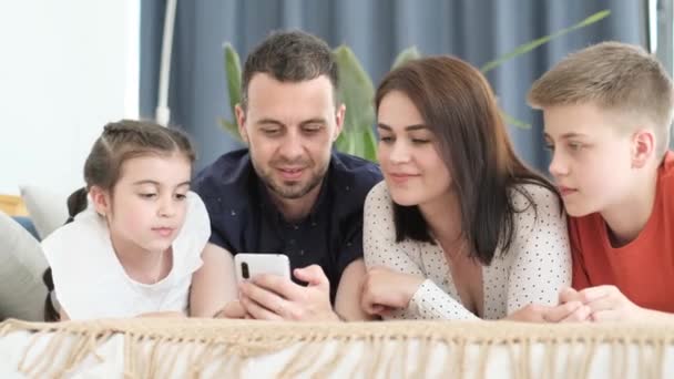 Buona famiglia americana che si rilassa sul divano di casa, usa lo smartphone e si diverte a ridere. Tutta la famiglia insieme a casa - Filmati, video