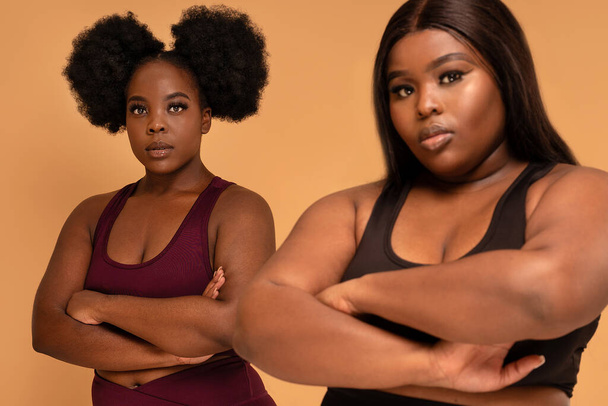 Active two plus size femal fitness trainers posing in fashionable sporty clothes together, looking at the camera. Real people lifestyle. Gym, healthy lifestyle concept. Body acceptance. - Foto, imagen