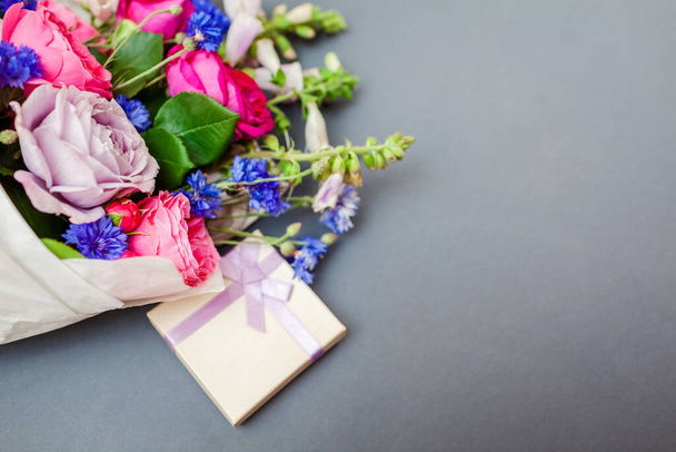Detailní záběr na letní kytice růží liščí rukavice bakalářské knoflíky květiny zabalené v papíru a uspořádány na pozadí s dárkovou krabicí. Dárek k dovolené - Fotografie, Obrázek