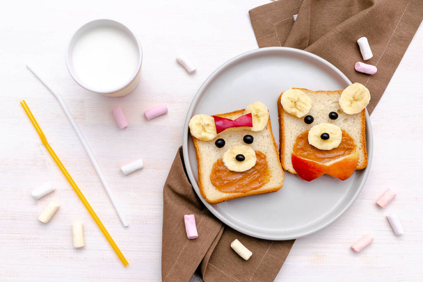 Engraçado urso bonito, cara de cachorro pão de sanduíche com manteiga de amendoim, banana, maçã, leite, marshmallow. Crianças crianças bebê doce sobremesa saudável almoço comida arte no prato, close-up, vista superior. - Foto, Imagem