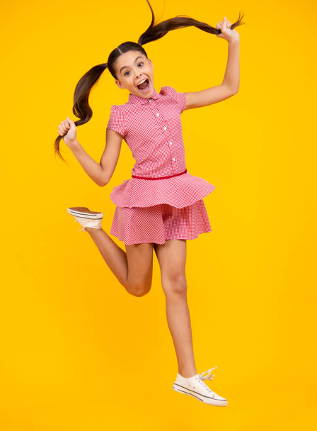 Pleine longueur ravi adolescent gamin fille 12 13 14 ans sautant vieux isolé sur fond jaune studio. Drôle de saut. Enfant en robe de mouvement d'été - Photo, image