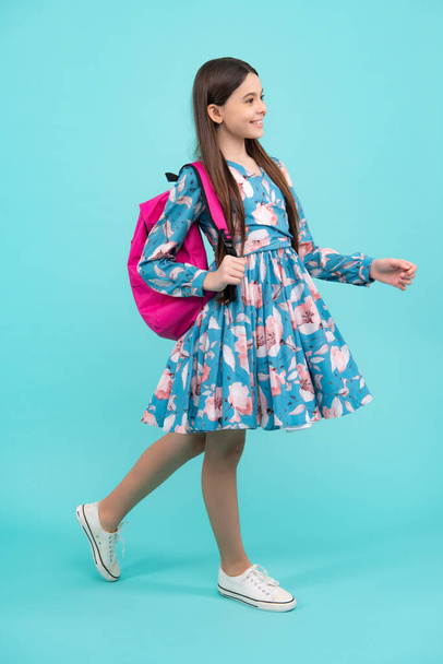 Chica de la escuela en uniforme escolar con bolsa de la escuela. Adolescente escolar sostiene la mochila sobre fondo azul aislado. Adolescente feliz, emociones positivas y sonrientes - Foto, imagen