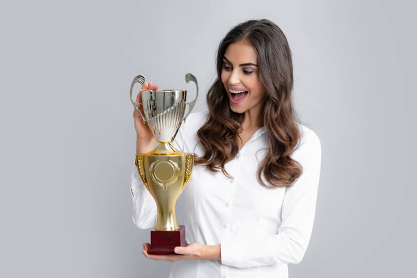 Winning businesswoman holding a trophy. Business woman with prize. Business woman with golden cup and fist up gesturing, isolated on gray. Concept of victory and success - Photo, image
