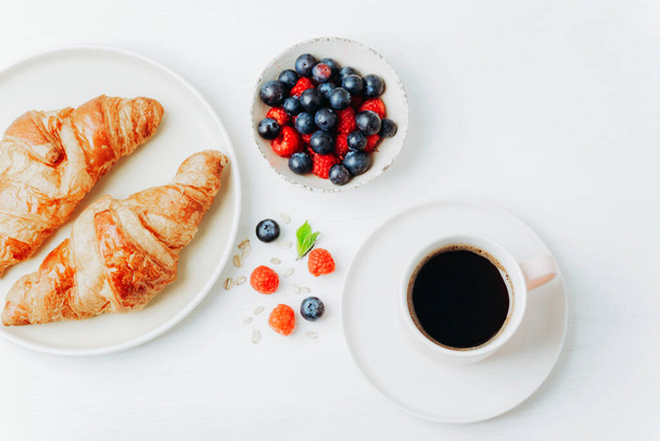 Kaffee, Croissants und Beerenfrühstück auf einem weißen Tisch. Draufsicht, flache Lage. - Foto, Bild