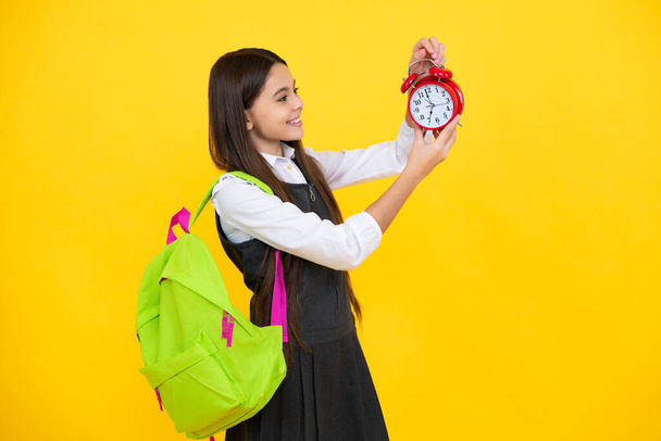 Zurück zur Schule. Teenager-Schülerin mit Rucksack hält Wecker, Zeit zum Lernen. Schulkinder auf gelbem Hintergrund. Glückliches Mädchengesicht, positive und lächelnde Emotionen - Foto, Bild